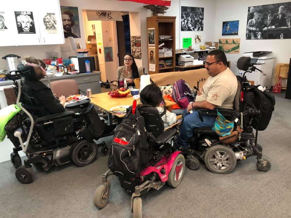 Four people in a wheelchair sit around a table having a discussion